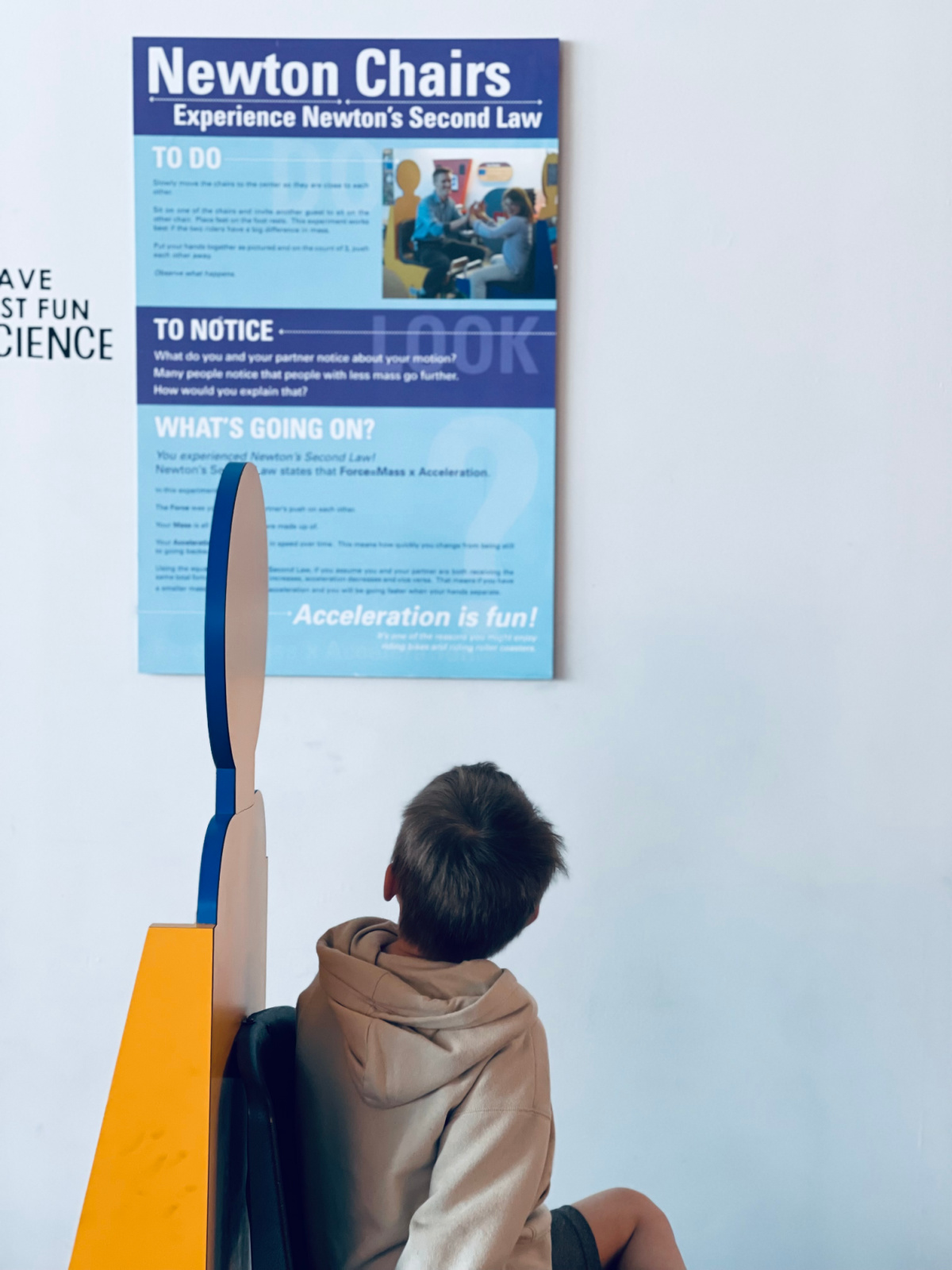 young boy at science museum looking at poster on the wall explaining Newton's Second Law.