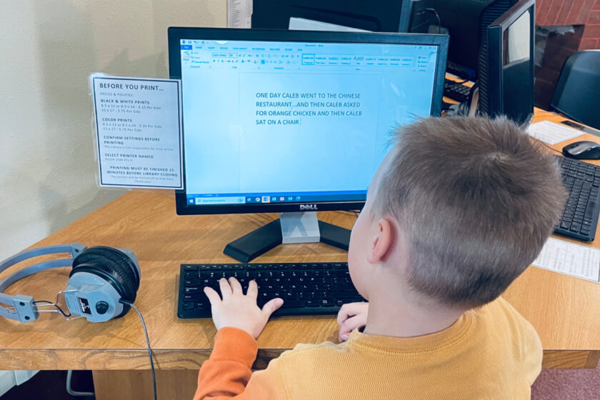 unschooled child writing stories on the computer at local library.