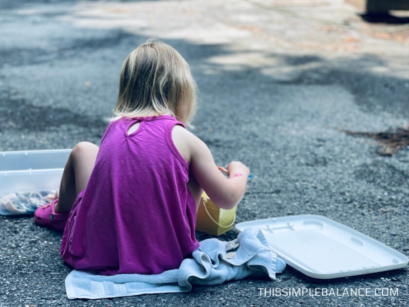 preschooler outside on driveway cleaning shells.