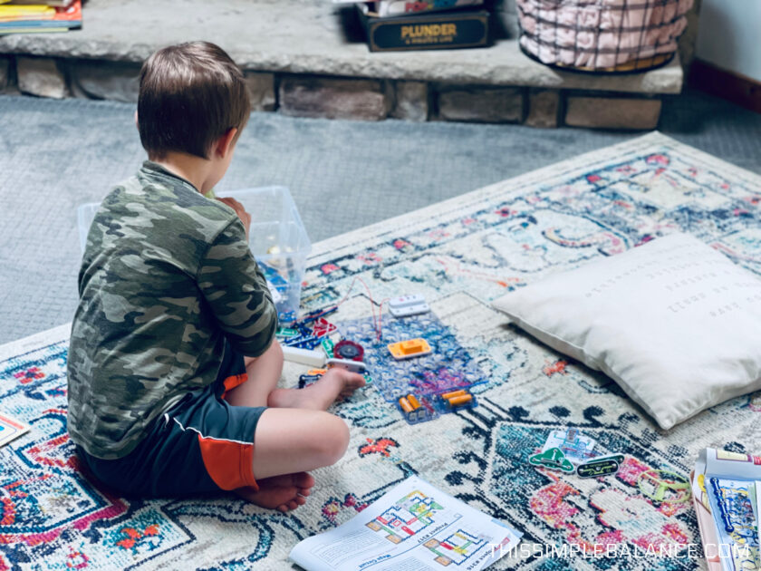 young child playing with Snap Circuits on living room rug.