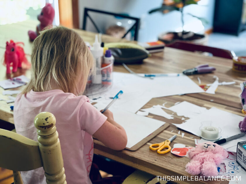 4 year old girl sitting at kitchen table drawing and cutting paper