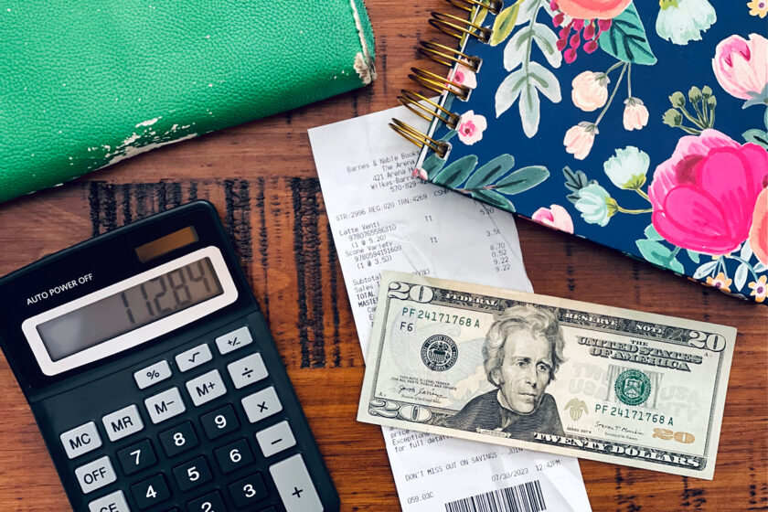 calculator, wallet, receipt and $20 bill sitting on table with colorful notebook.