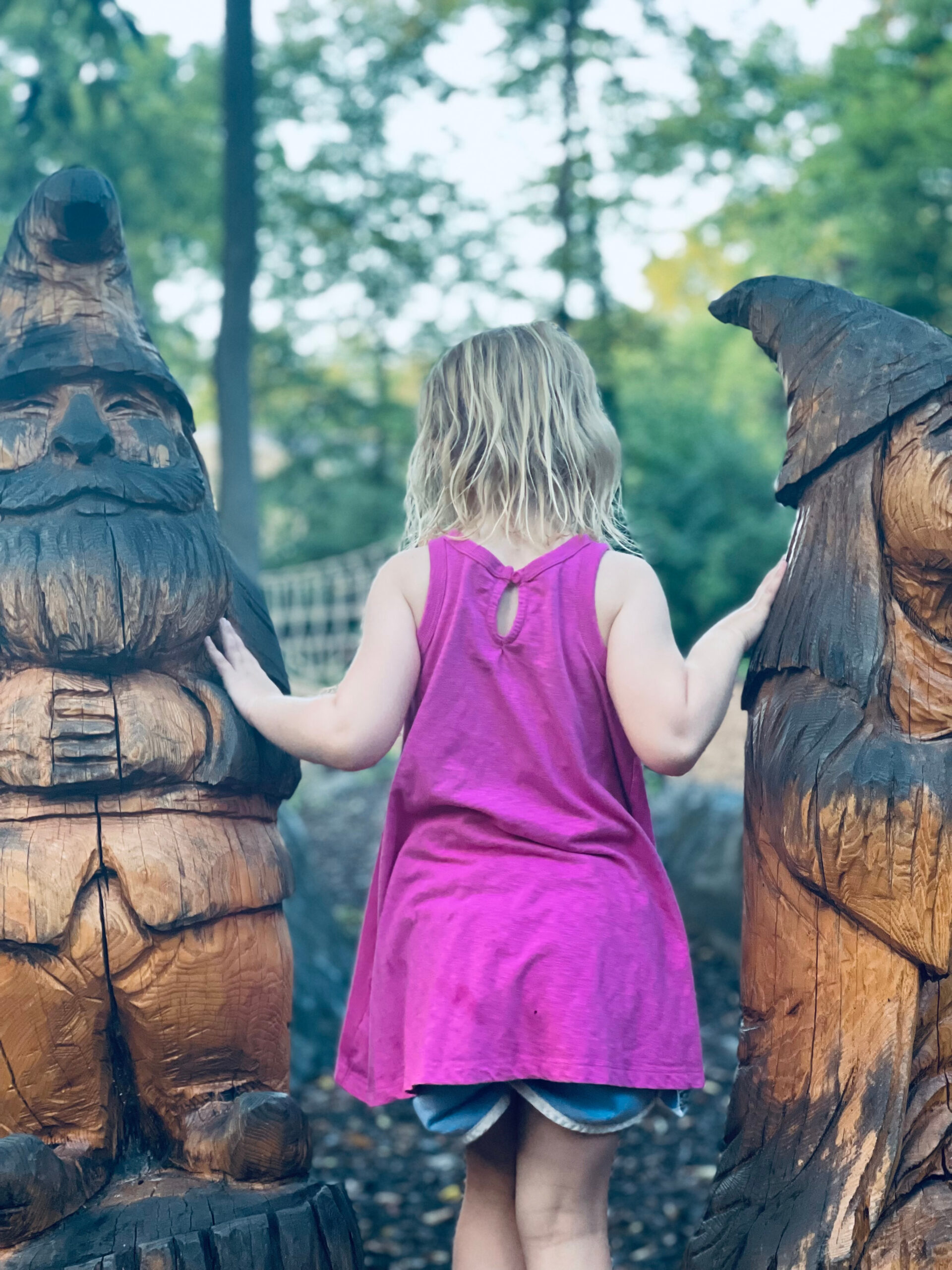 unschooled child standing between two wooden statues at a local park.
