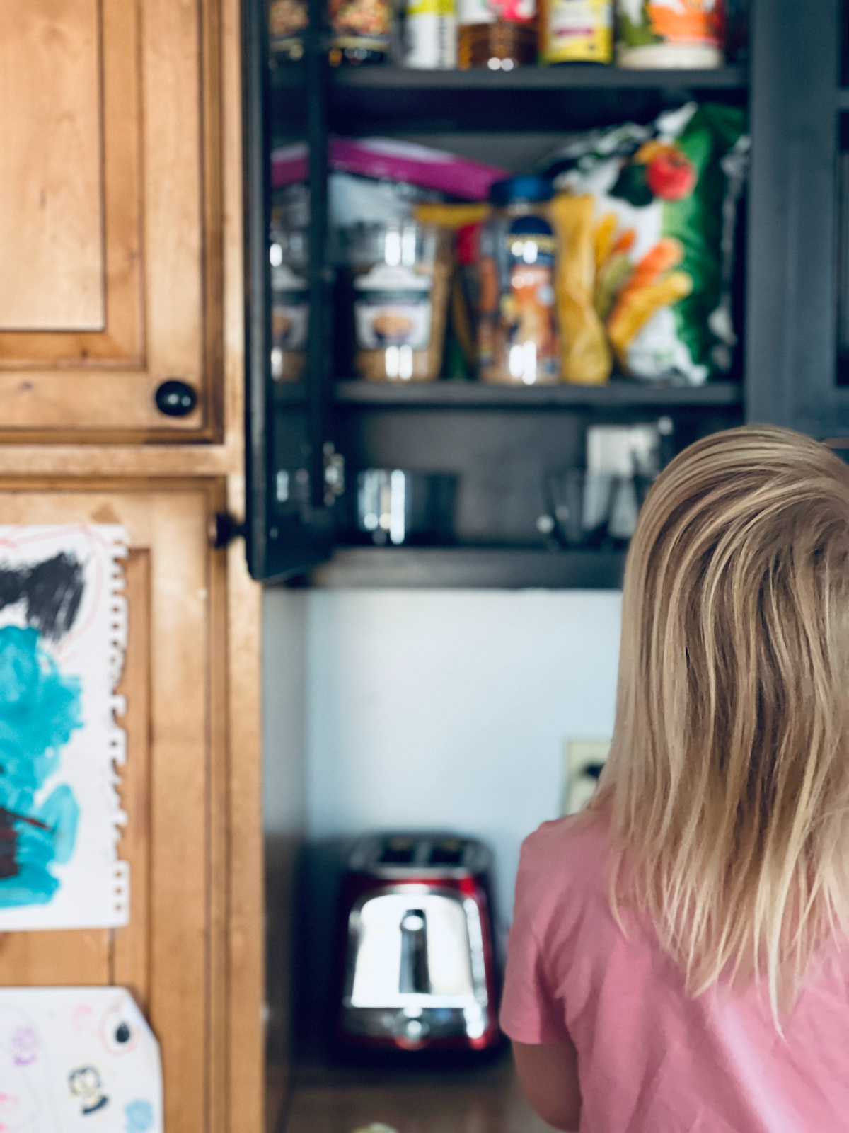 young girl looking at open cabinet with snacks