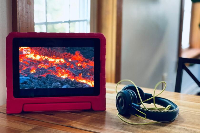 ipad showing erupting volcano sitting on table with headphones.