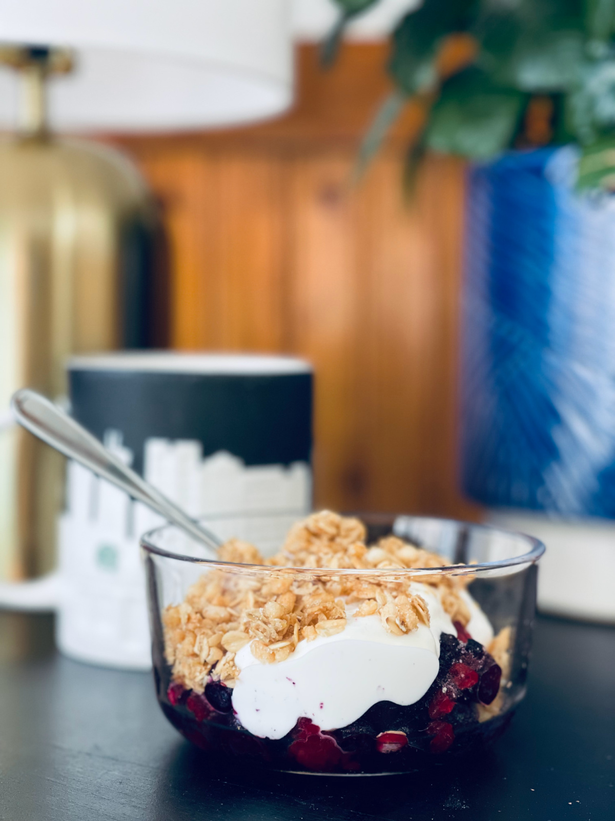 Yogurt parfait close up, with coffee mug and plant in background.