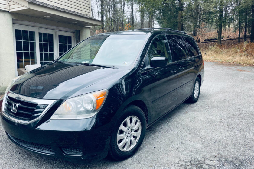 older black Honda Odyssey minivan in driveway in front of house.