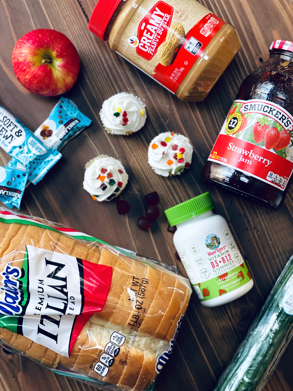 flat lay with bread, vitamins, granola bars, apples, cupcakes, peanut butter and jelly.