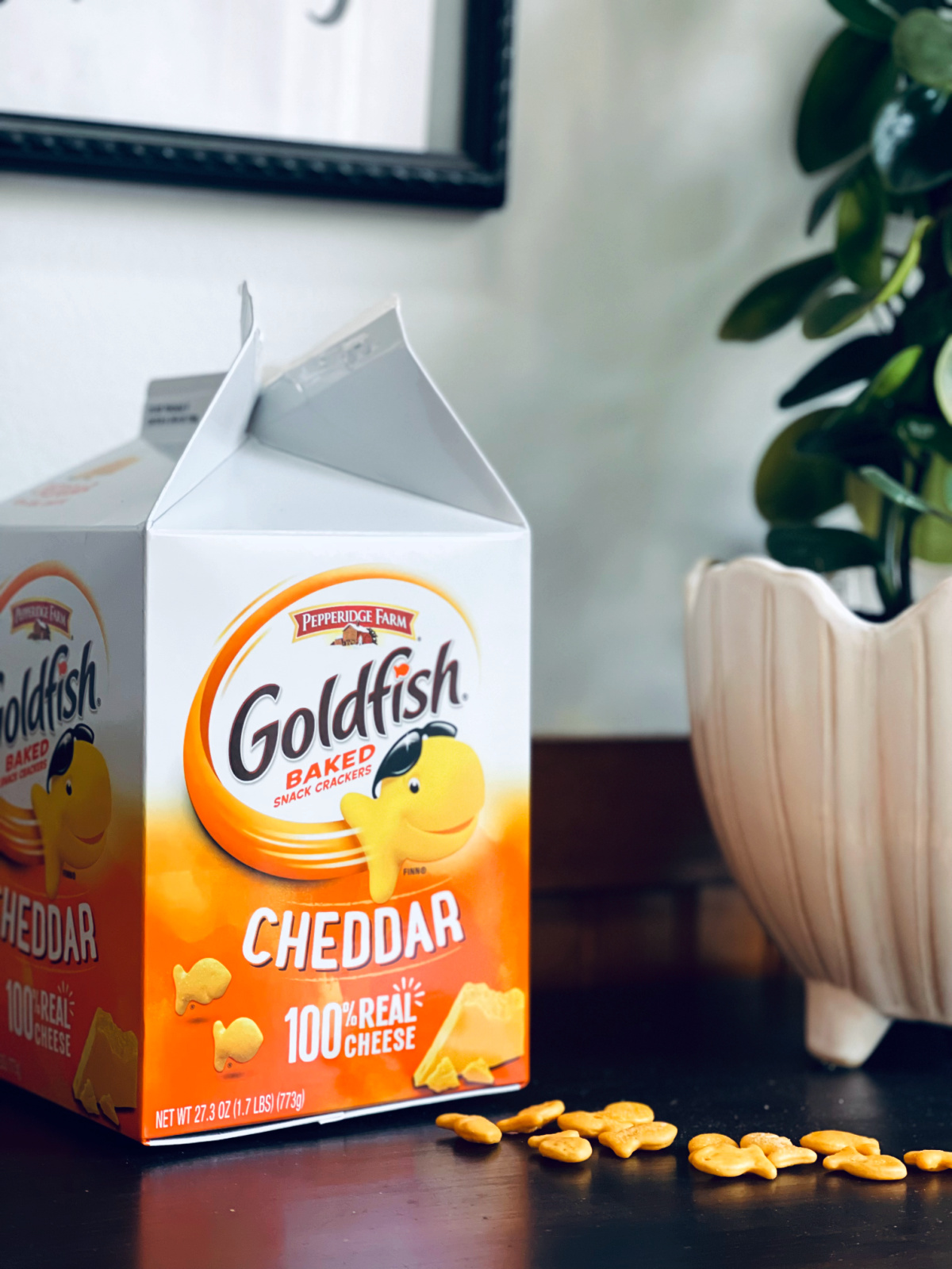 Pepperidge Farm goldfish box with goldfish scattered on table and plant in background.