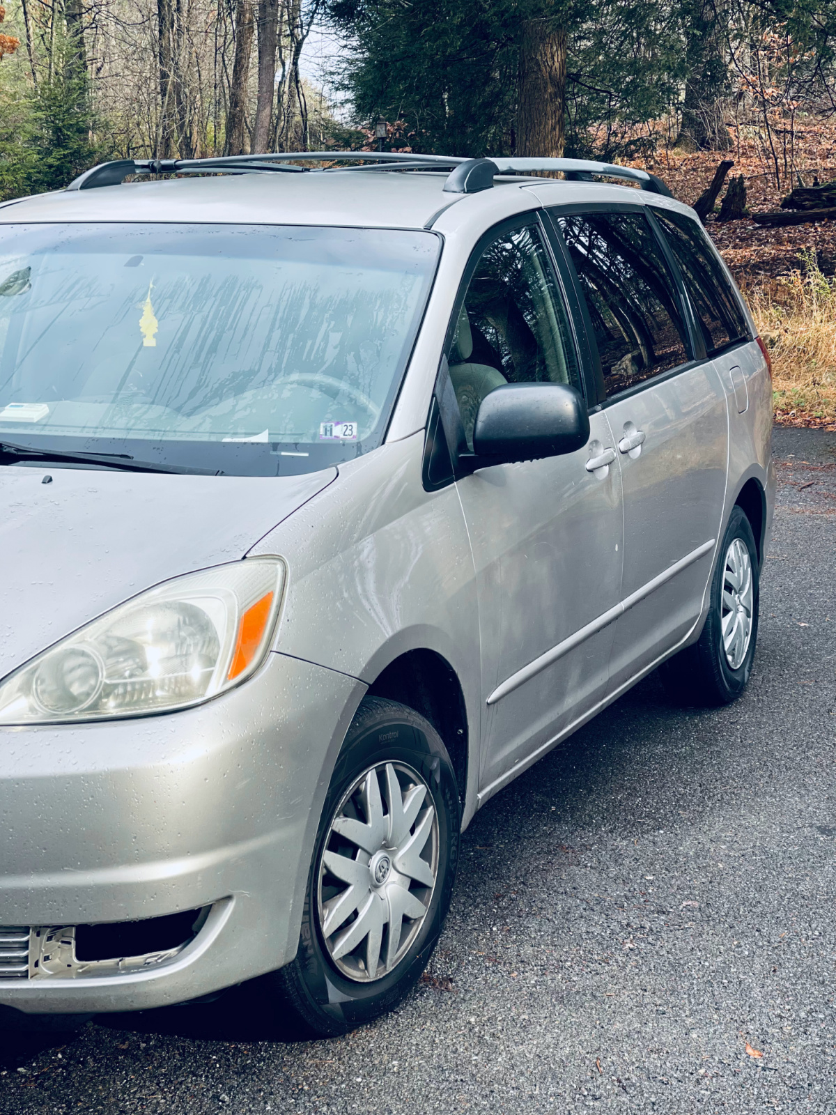 silver Toyota Sienna minivan in driveway with woods behind it