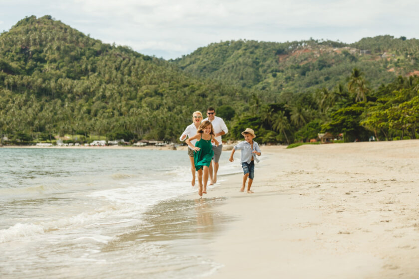 family running on the beach together, smiling and happy.