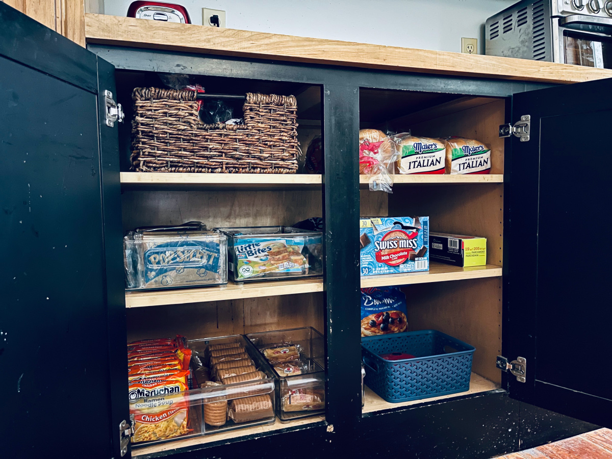 pantry cabinets with snacks in plastic bins, hot chocolate and bread.