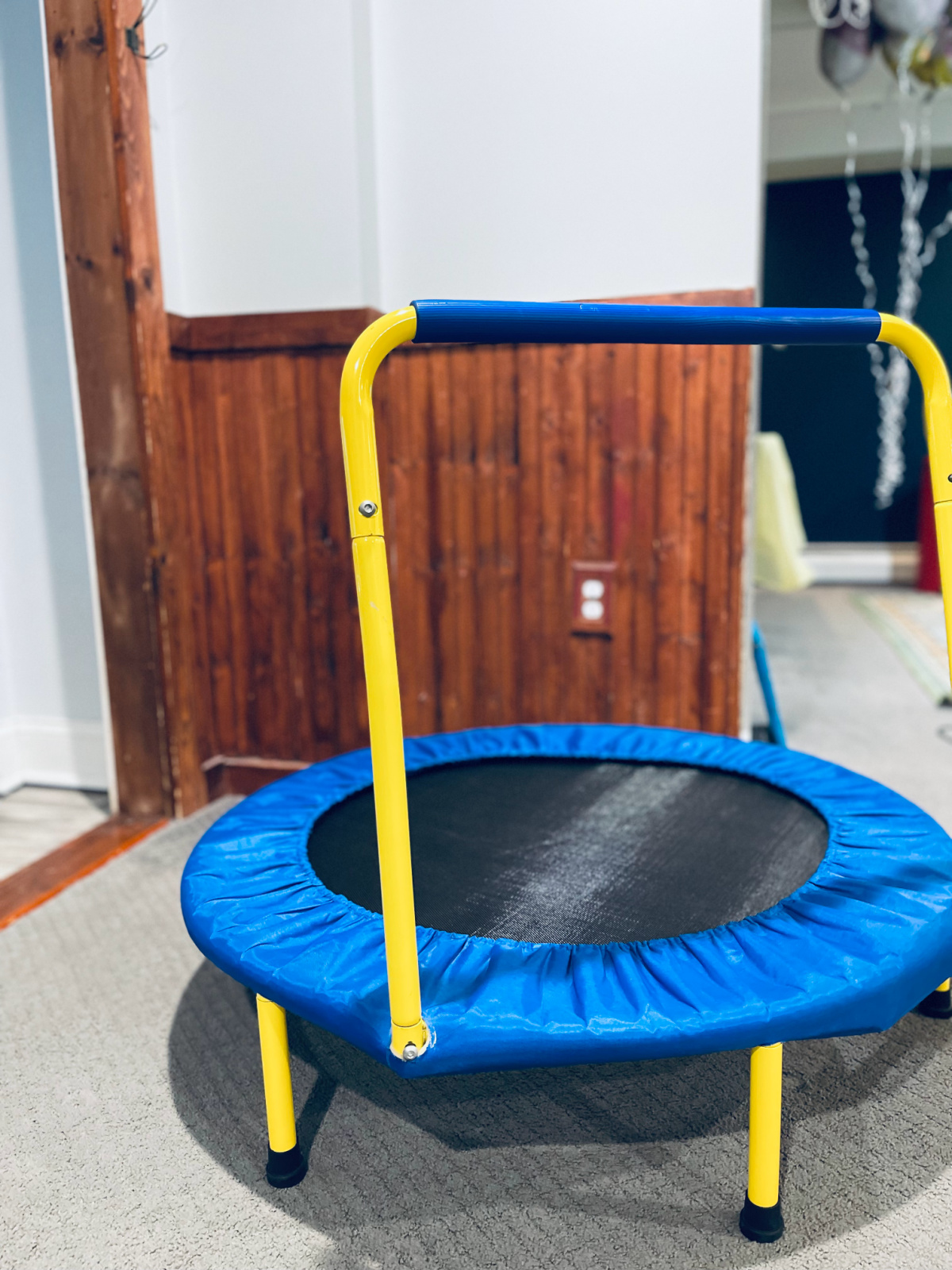small indoor trampoline with support bar for kids in playroom.