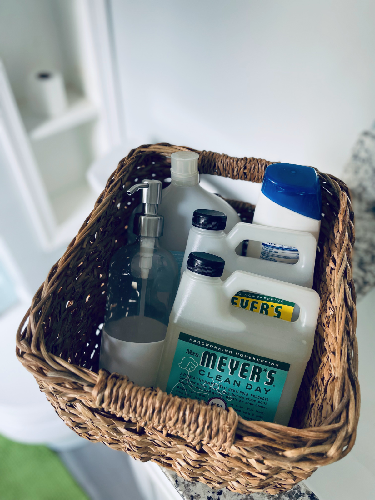 basket with Mrs. Meyer's hand soap refills and glass soap dispenser in bathroom.