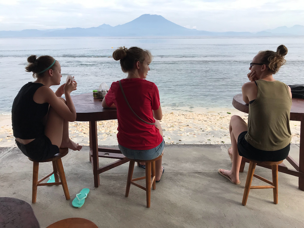 Marla Taviano's unschooled daughters sitting at a beach overseas.
