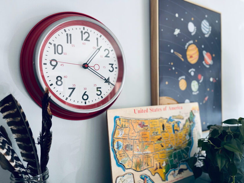 clock on the wall next to canvas painting of the planets and United States of America puzzle.