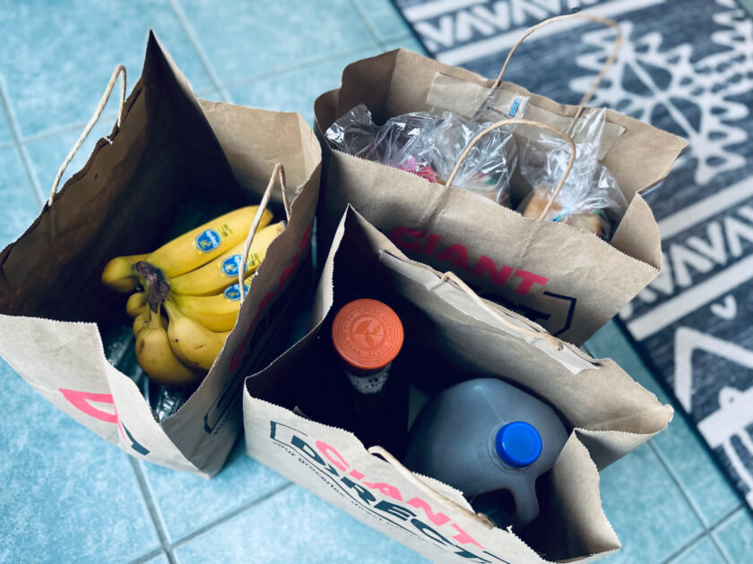 grocery bags on floor, showing contents like bananas and gallons of tea.