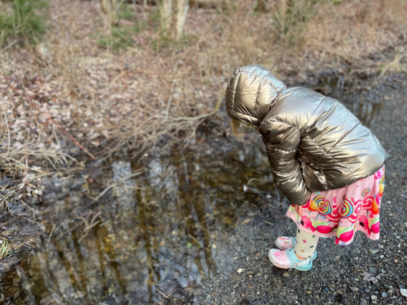girl with gold coat and colorful clothes staring at reflections in puddles.