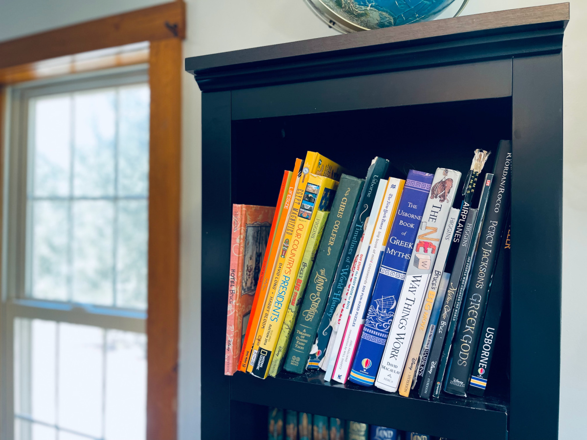 assorted homeschool reference books on black bookshelf near window.
