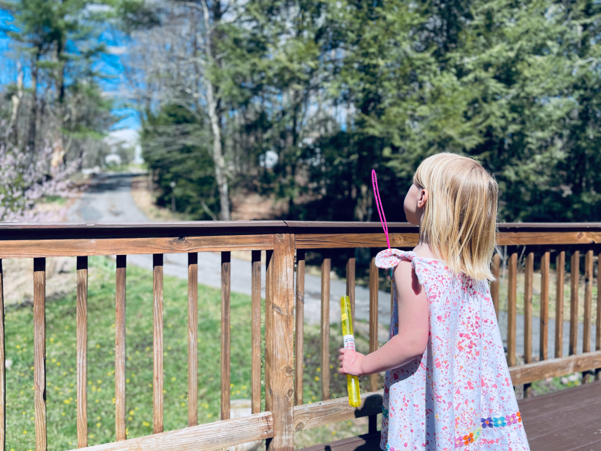 little girl blowing bubbles on deck in the spring.