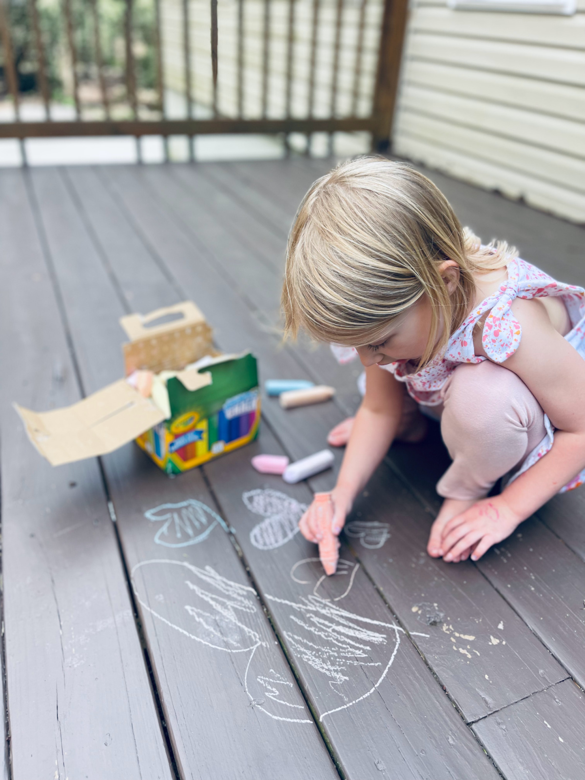 child drawing with Crayola chalk on a deck.