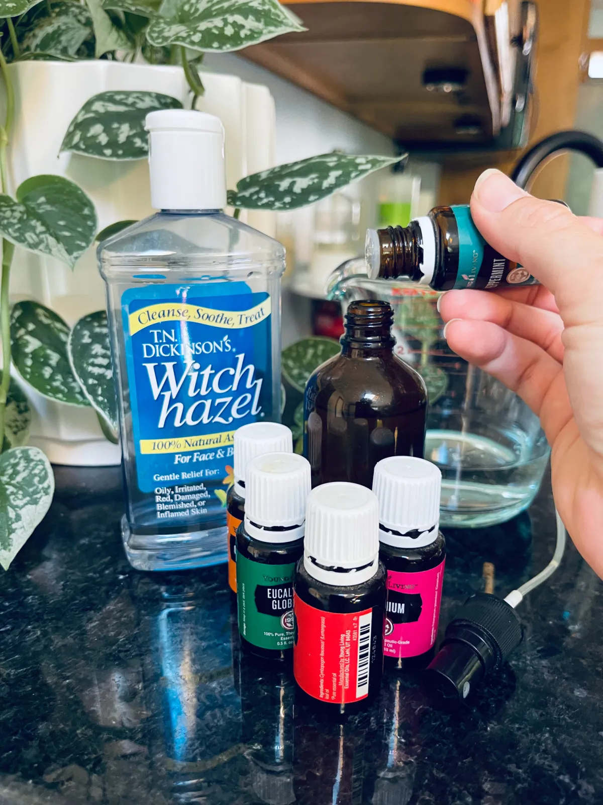 adding drops of essential oil to amber spray bottle with other ingredients in background.