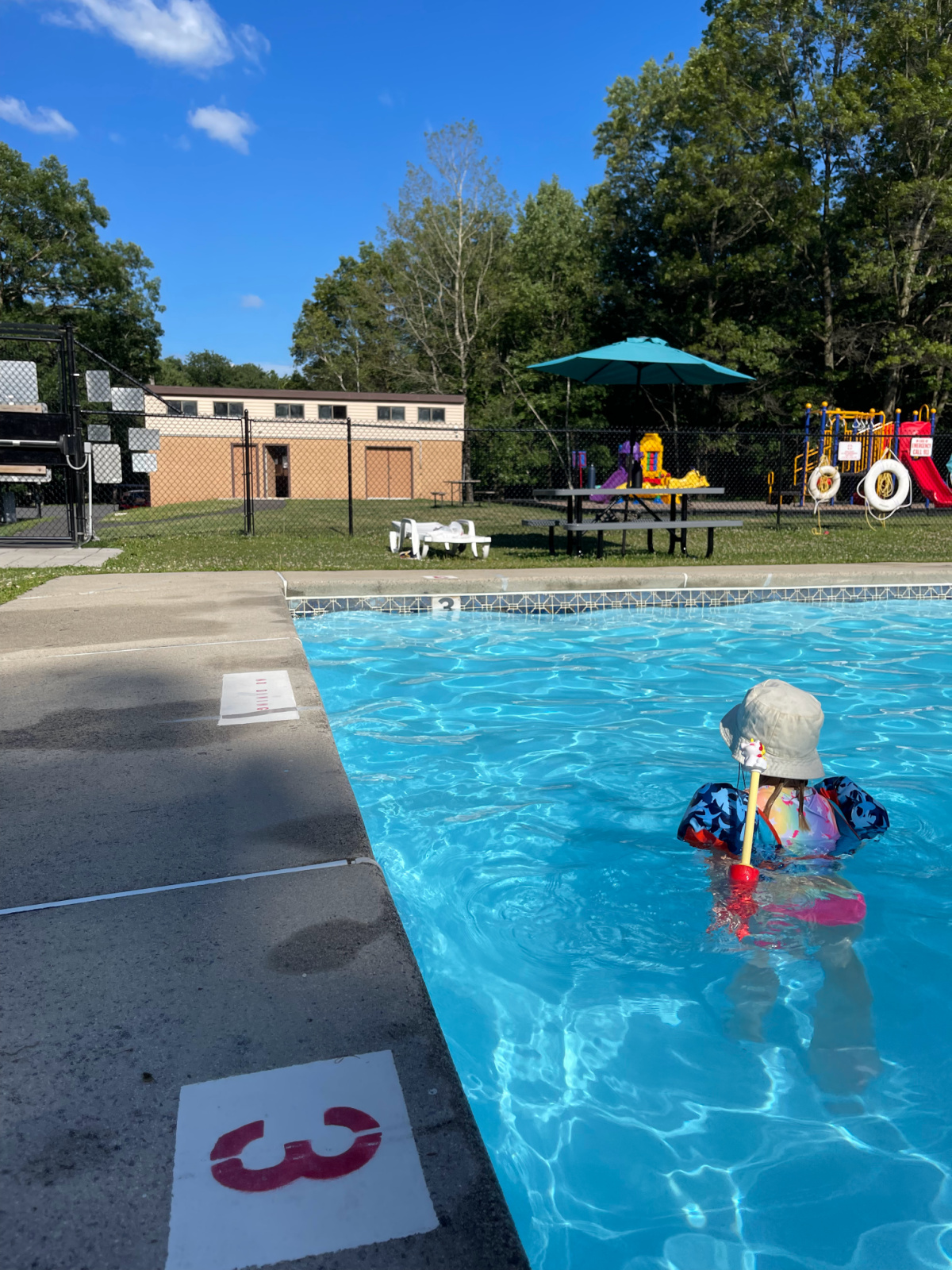 small child with floaties swimming in a pool next to a playground.