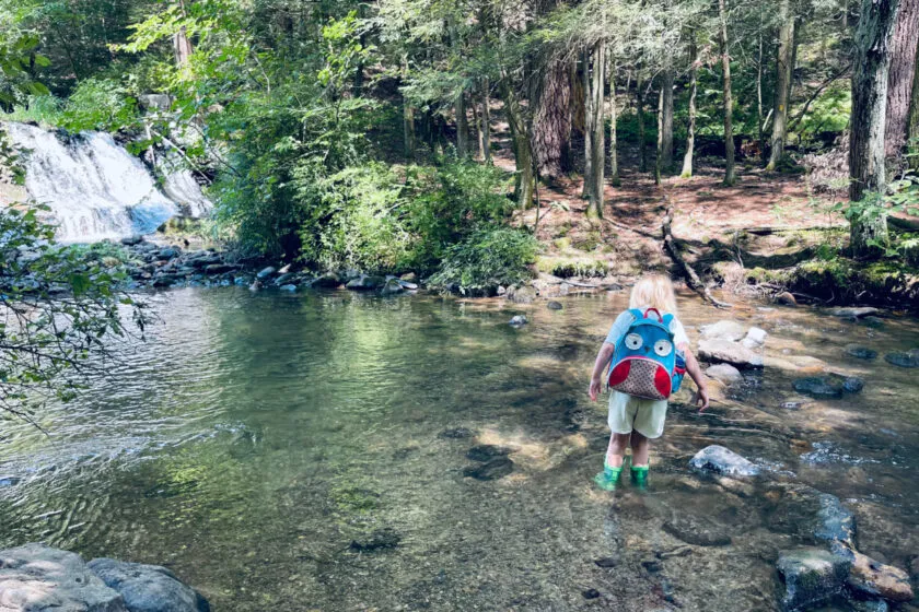 unschooled child playing in a creek near a waterfall.