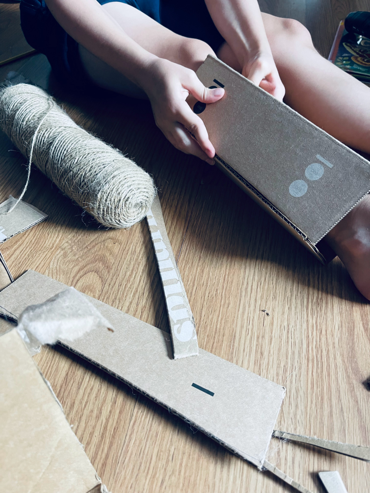 child creating cardboard armor, putting cardboard on leg.
