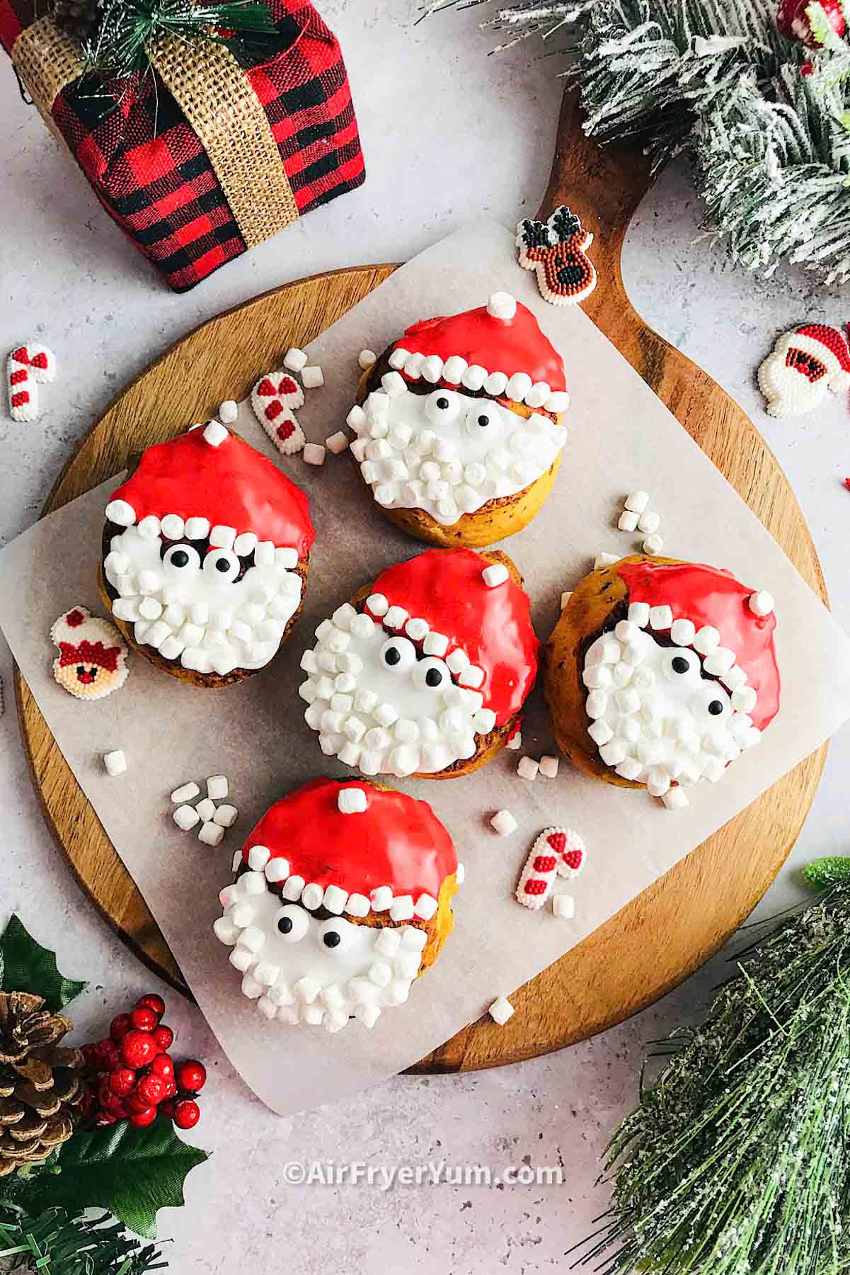 air fryer santa cinnamon rolls on parchment and cutting board with holiday themed photo.