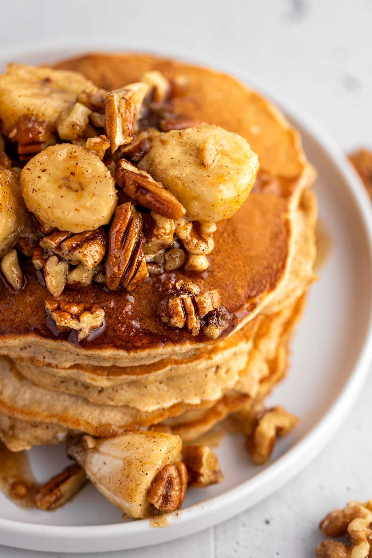 banana fosters pancakes up close with bananas, walnuts and syrup in focus.