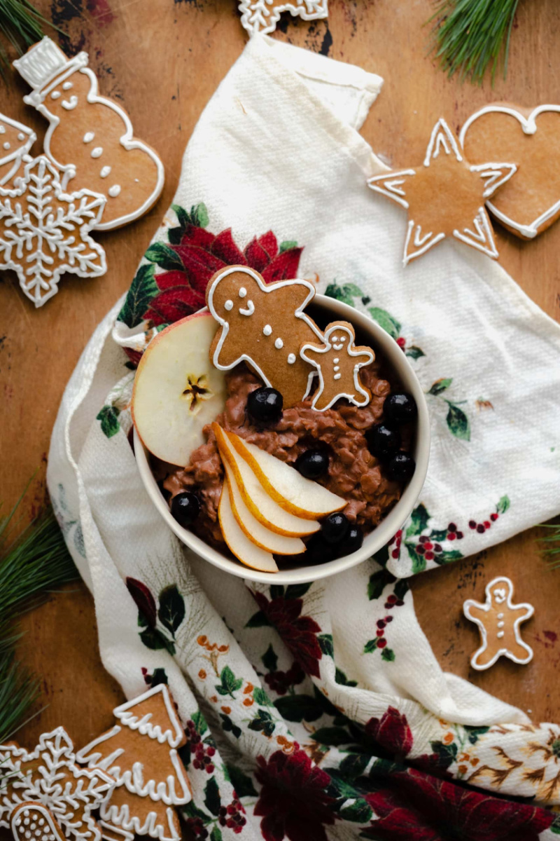 chocolate gingerbread in bowl with apple slices and gingerbread cookies on Christmas tea towel.