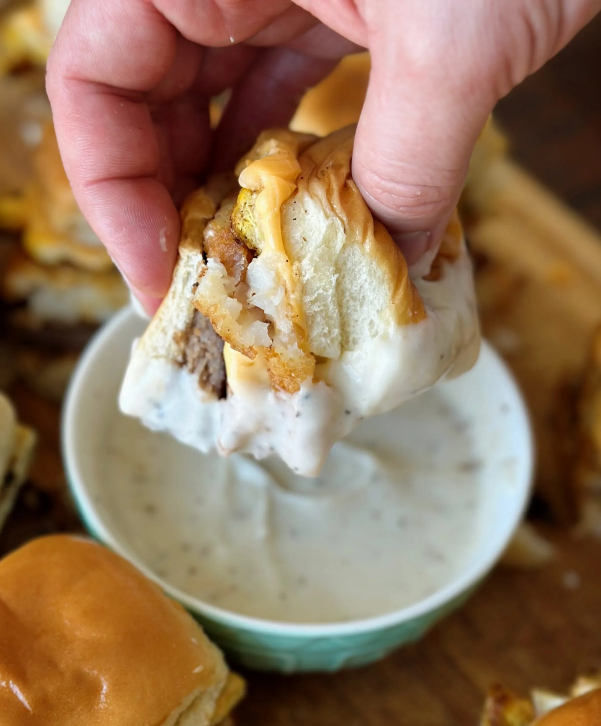 breakfast slider sandwich being dipped in a bowlful of country gravy.