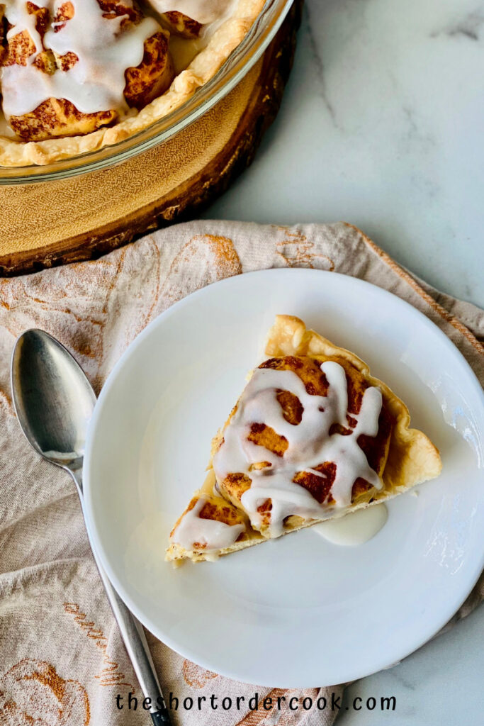 slice of cinnamon roll pie on white plate with spoon next to it.