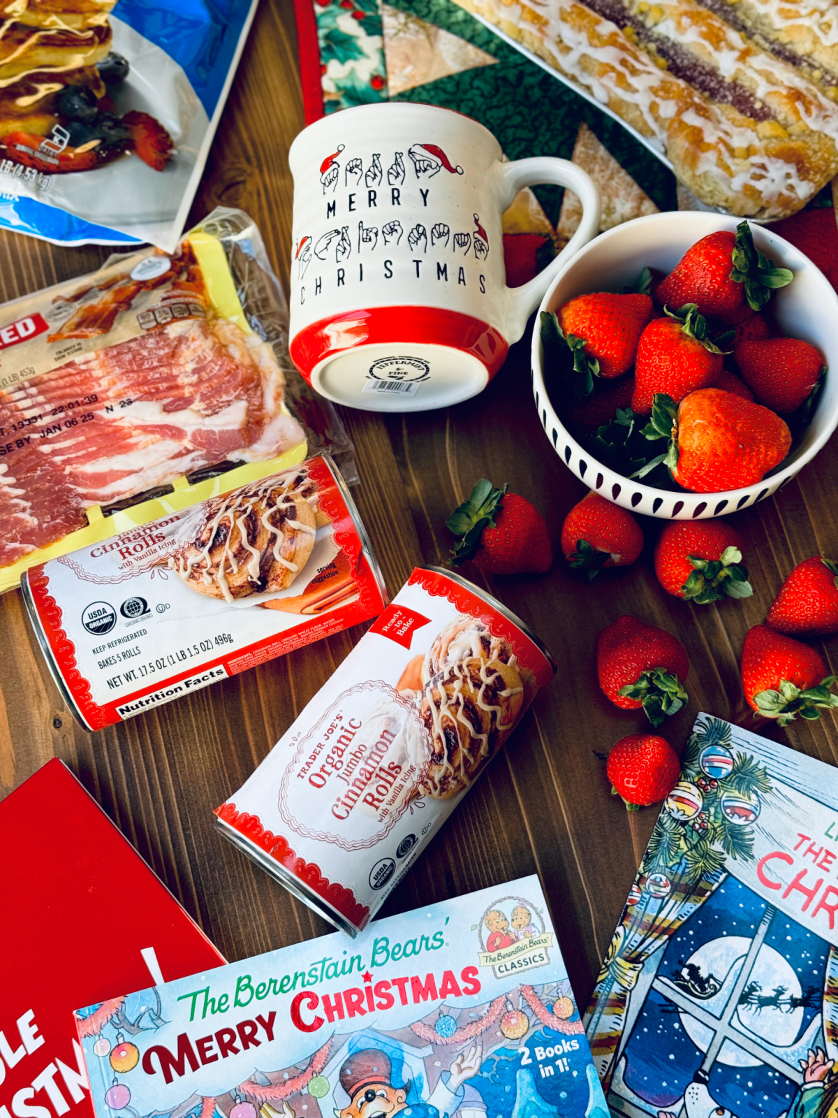 Christmas morning breakfast items flat lay with strawberries, danish, bacon, Trader Joe's cinnamon rolls and Merry Christmas mug.
