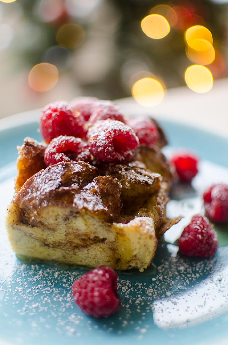 slice of overnight eggnog french toast topped with syrup and raspberries for Christmas morning.