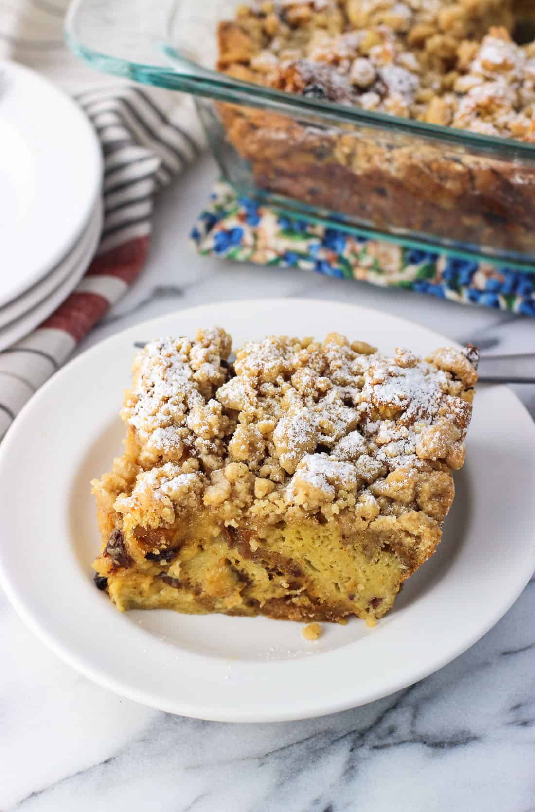 A slice of baked panettone french toast on a white plate with casserole dish in background.