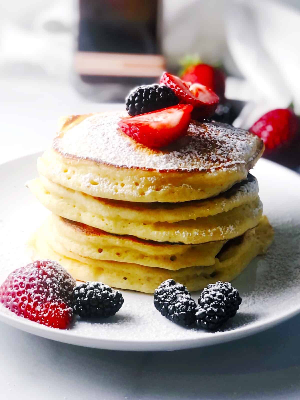 ricotta pancakes stacked with berries and powdered sugar on top.