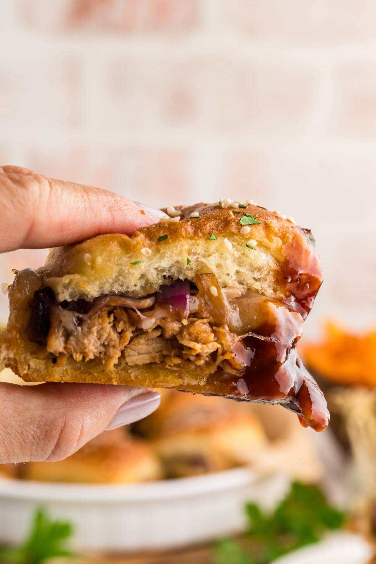 close up on hand holding chicken sliders with barbecue sauce.