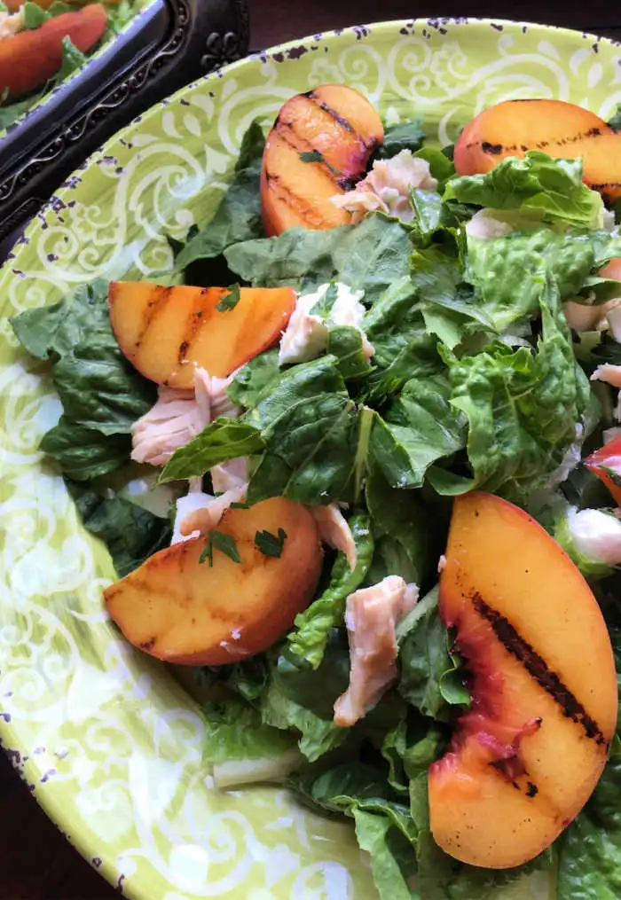 grilled peaches on top of rotisserie chicken salad on colorful green plate with dressing.