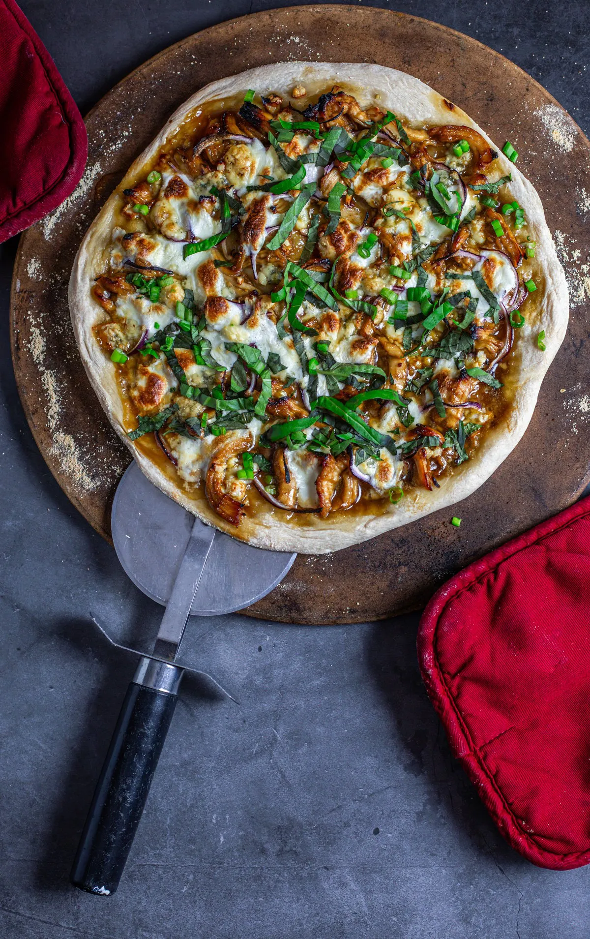 hot honey pizza on pizza stone with red potholders and pizza cutter underneath the edge.