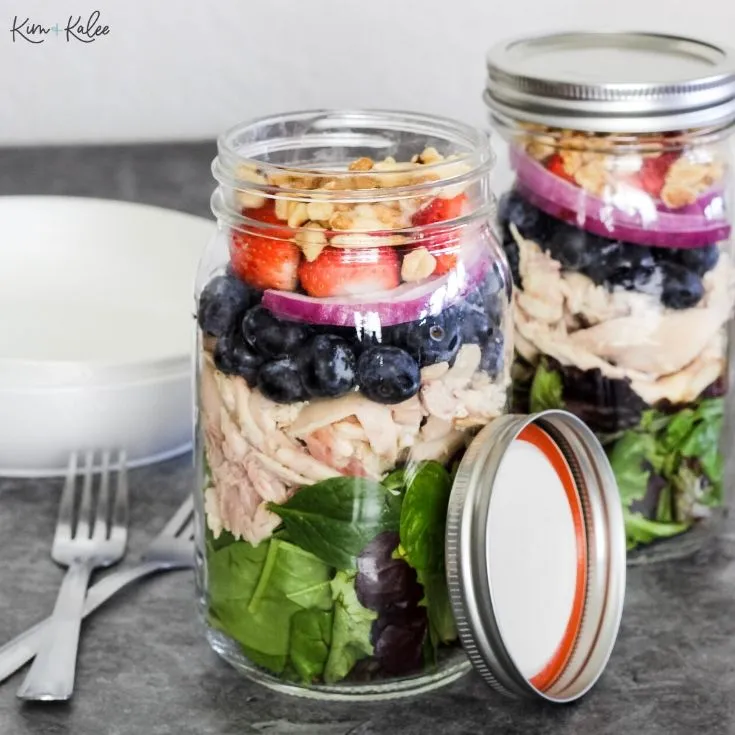 layered strawberry chicken salad with blueberries in mason jars.