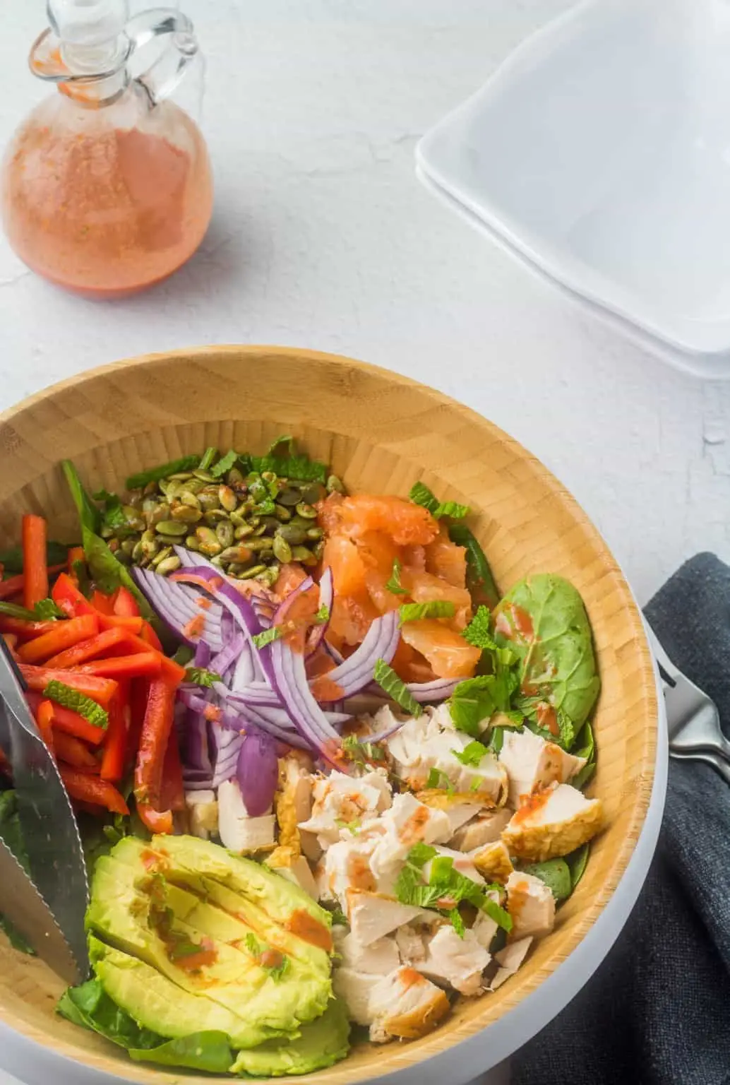 chipotle chicken spinach salad in large wooden bowl with salad dressing in background.