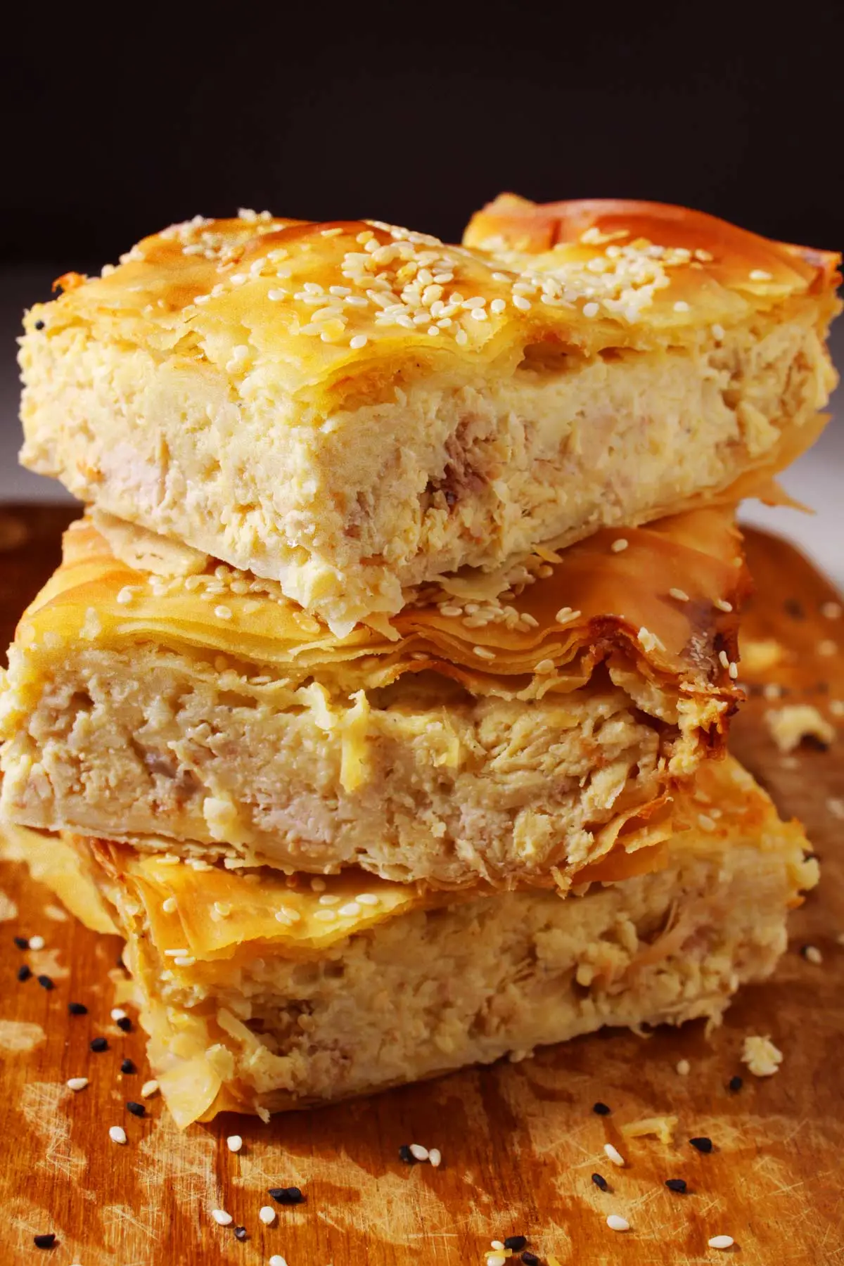 slices of chicken pot pie with phyllo dough stacked on cutting board, sprinkled with sesame seeds.