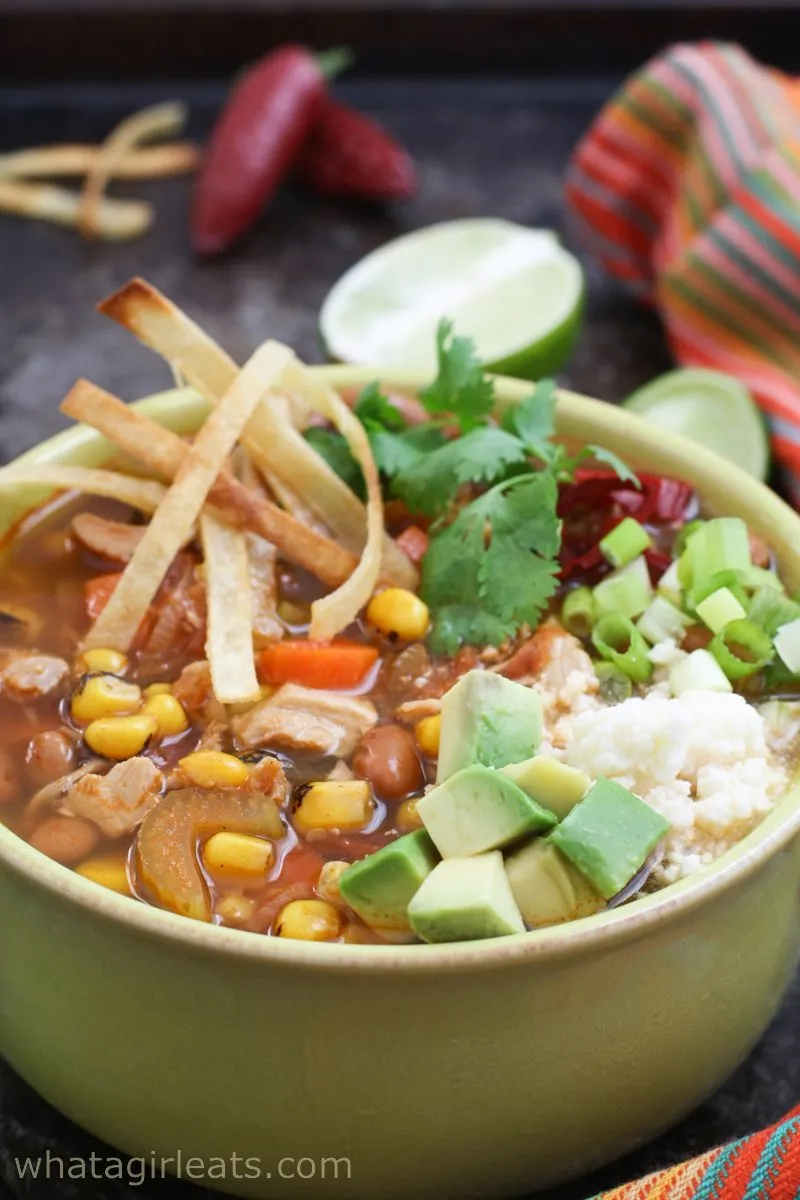 chicken tortilla soup in green bowl with toppings.