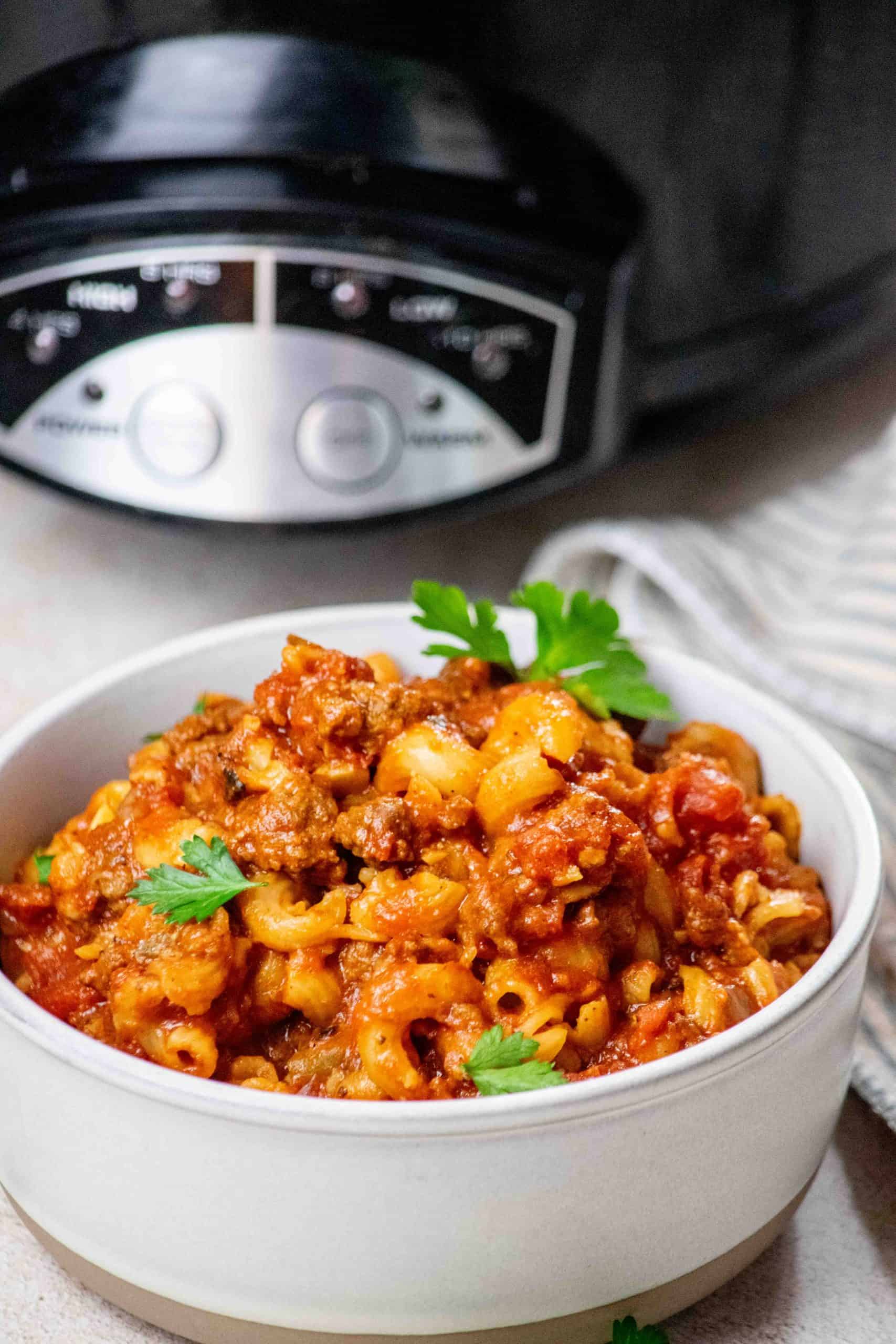 American beef goulash in white bowl with crockpot in the background.