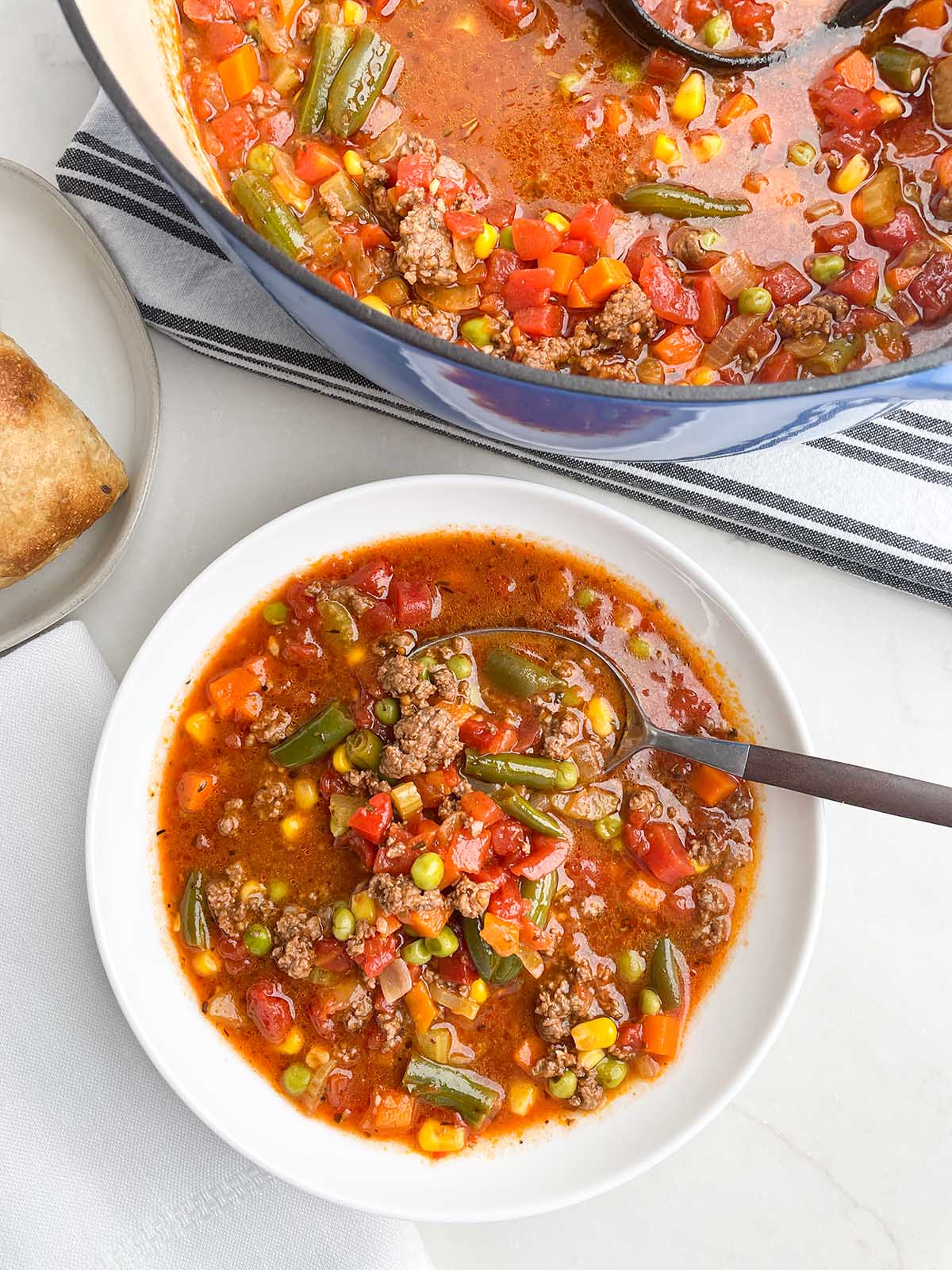 easy ground beef vegetable soup in white bowl with spoon, soup pot in background.