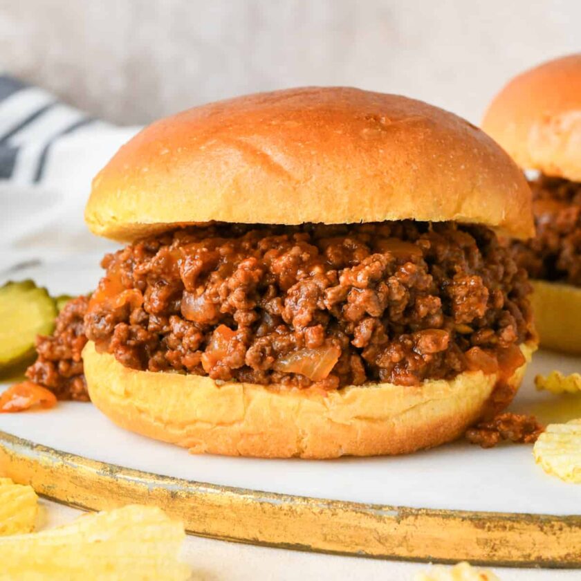 homemade sloppy joe on a hamburger bun, with pickles nearby.