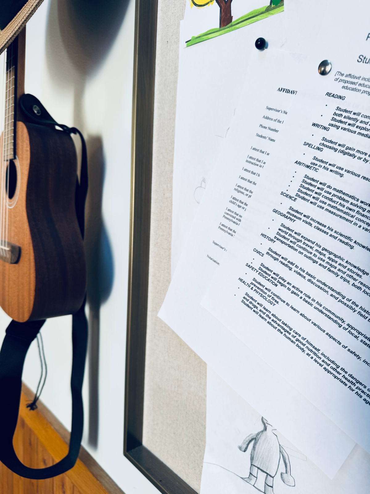 homeschooling affidavits and objectives hanging on bulletin board with ukulele in background.