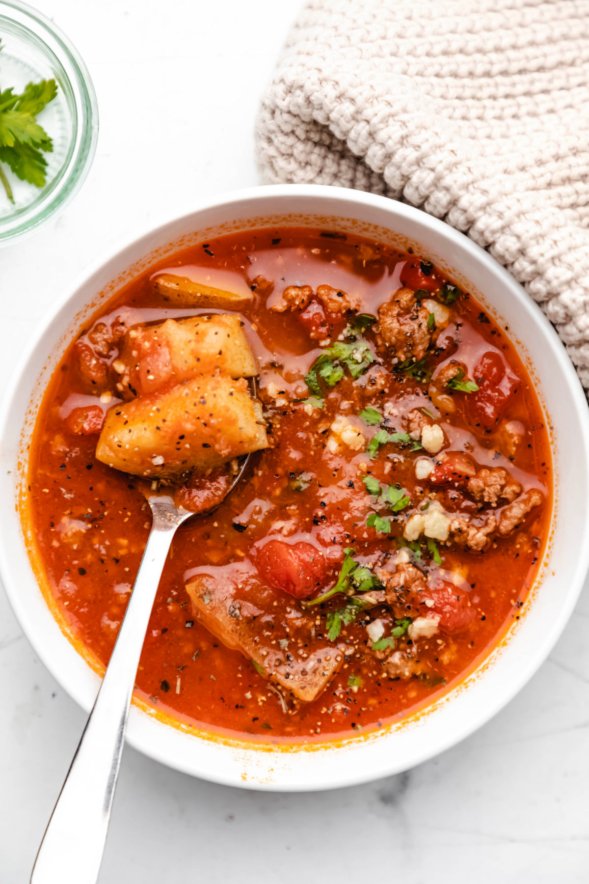 serving of instant pot hamburger soup in white bowl with spoon and off white dish towel.